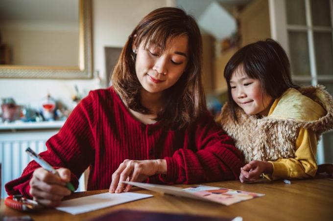 jeune jolie maman écrivant une carte de voeux pour la famille avec sa charmante fille à la maison