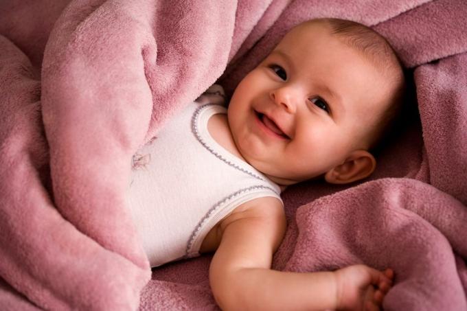 portrait de bébé dans une chemise blanche de style débardeur souriant et enveloppé dans une couverture rose tendre