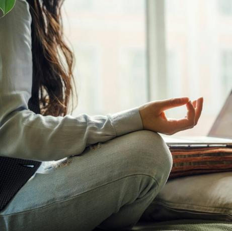 une femme asiatique d'âge moyen en jeans bleus assise sur le lit dans une pose de yoga devant un ordinateur portable travaillant à distance à la maison faisant des achats en ligne pendant la période de quarantaine