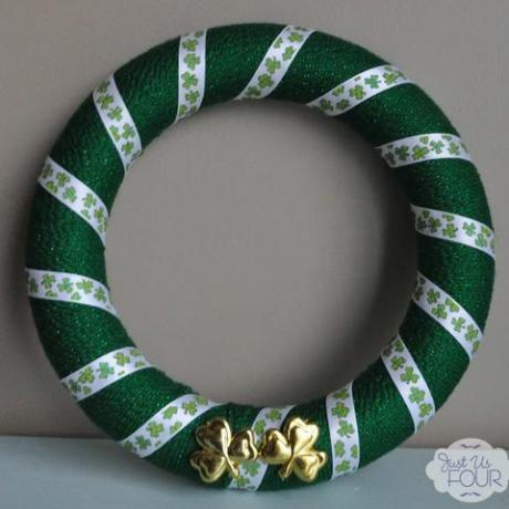 couronne ronde enveloppée de fil vert avec un ruban imprimé trèfle dessus et deux trèfles dorés au bas de la couronne