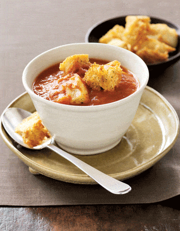 petit bol de soupe aux tomates avec croûtons sur soucoupe avec cuillère