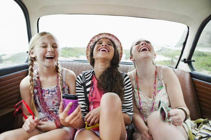 trois filles rient sur la banquette arrière d'un véhicule