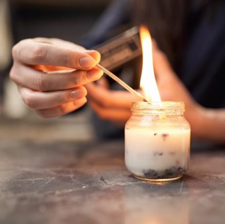 récolter une femme anonyme avec une allumette brûlante allumant une bougie aromatique dans un pot en verre placé sur une table en marbre à la maison