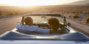 vue arrière du couple en voyage sur la route conduisant une voiture décapotable classique vers le coucher du soleil