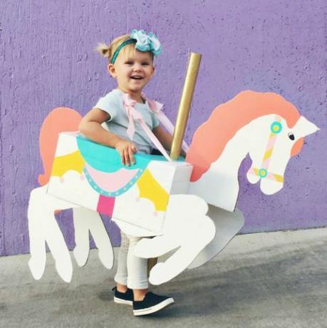 petite fille avec une boîte en forme et peinte pour ressembler à un cheval de manège autour d'elle
