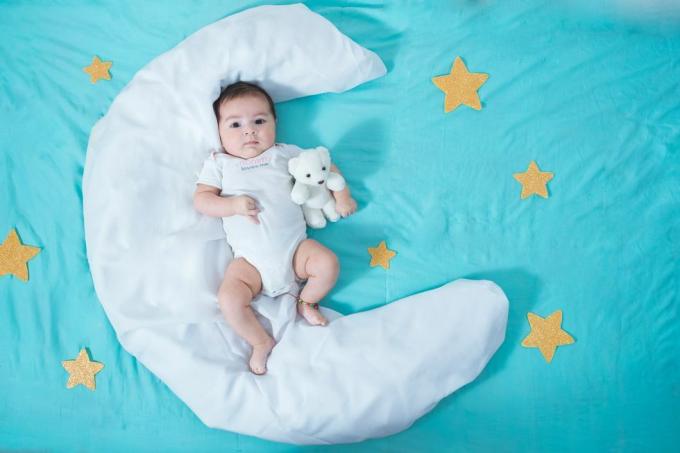 belle petite fille latine, âgée de deux mois, allongée sur un drap blanc en forme de lune avec des étoiles jaunes de chaque côté et un drap bleu en dessous