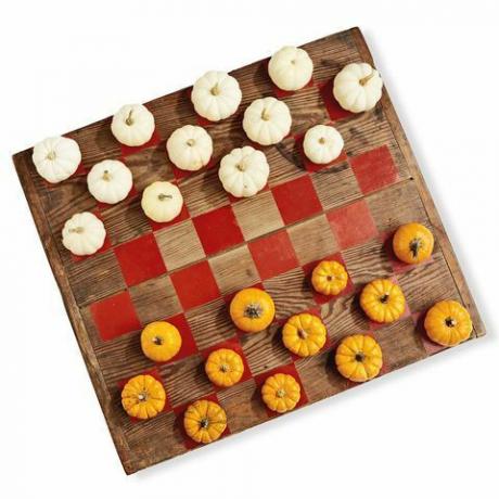 une planche de bois peinte comme un jeu de dames en utilisant des mini citrouilles en blanc et orange comme pièces de jeu