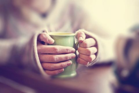 Tasse verte de boisson chaude détenue dans une paire de mains de la personne jumpered