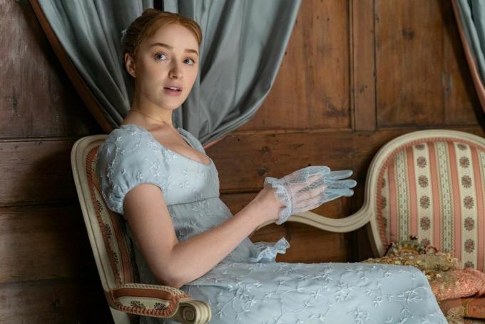 phoebe dynevor dans le rôle de daphne bridgerton dans l'épisode 102, assise, vêtue d'une robe bleue à taille empire