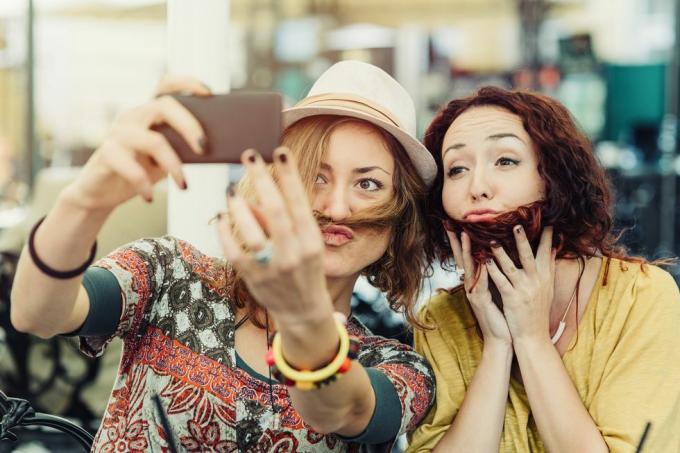 deux copines tenant les cheveux sur les visages pour avoir l'air d'avoir une barbe et une moustache et en prenant un selfie