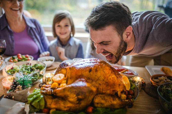 Jeune homme s'amusant sur le point de mordre une dinde farcie pendant le dîner de Thanksgiving dans la salle à manger