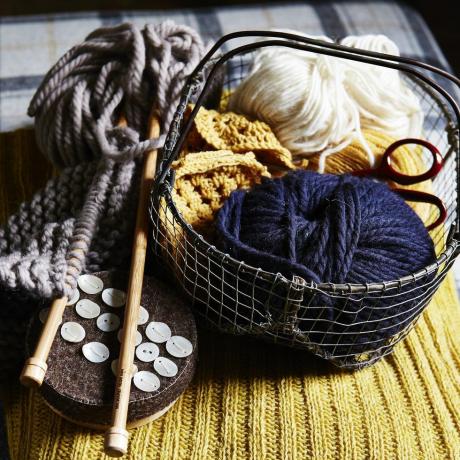 boules de laine bleue et blanche dans un petit panier métallique, aiguilles à tricoter en bois, boutons, placées sur un tissu tricoté côtelé jaune, texture