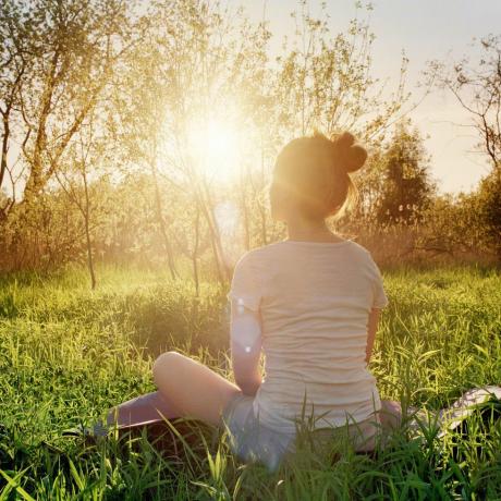 jeune femme assise en position de yoga profitant du coucher du soleil dans la nature
