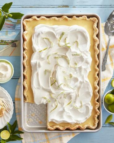 tarte à la dalle de citron vert dans une plaque à pâtisserie sur une table bleue avec de la crème fouettée et du citron vert confit sur le dessus