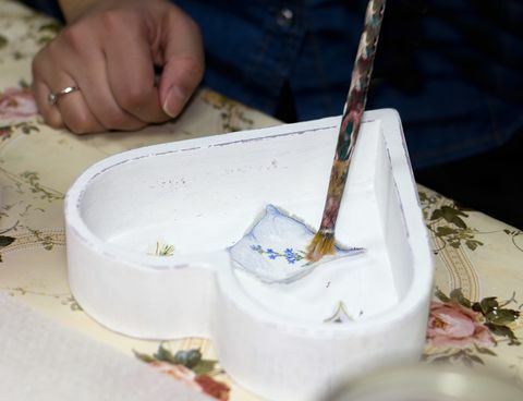 La main d'un artisan peignant une image découpée avec de la colle à l'intérieur d'une boîte blanche en forme de cœur