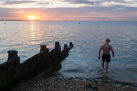 Alors que le soleil se couche sur la lumière du jour et les eaux calmes de l'estuaire de la Tamise, un nageur de mer sauvage entre dans l'eau pour son trempette régulière en soirée, le 18 juillet 2020, à whitstable, kent, angleterre photo de richard baker en images via getty images