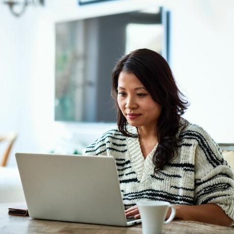 femme adulte d'une trentaine d'années assise à table et regardant un ordinateur, travaillant à distance, indépendante, petite entreprise