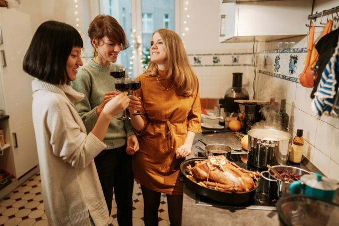 trois femmes boivent du vin rouge tout en préparant un repas de dinde à la maison avec une dinde et trois casseroles sur la cuisinière