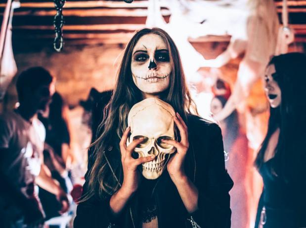 jeune femme avec maquillage squelette tenant le crâne à la fête d'halloween