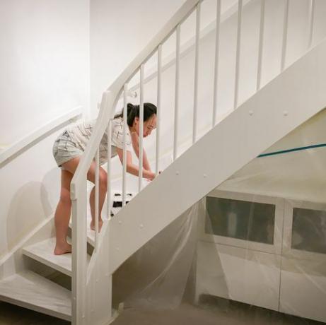 Femme appliquant de la peinture blanche fraîche à l'escalier